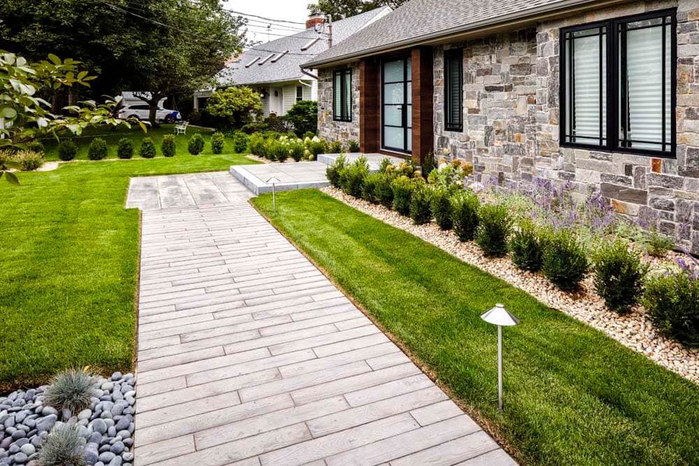 Clean long walkway approach with lawn, stone, low planting, and path lighting