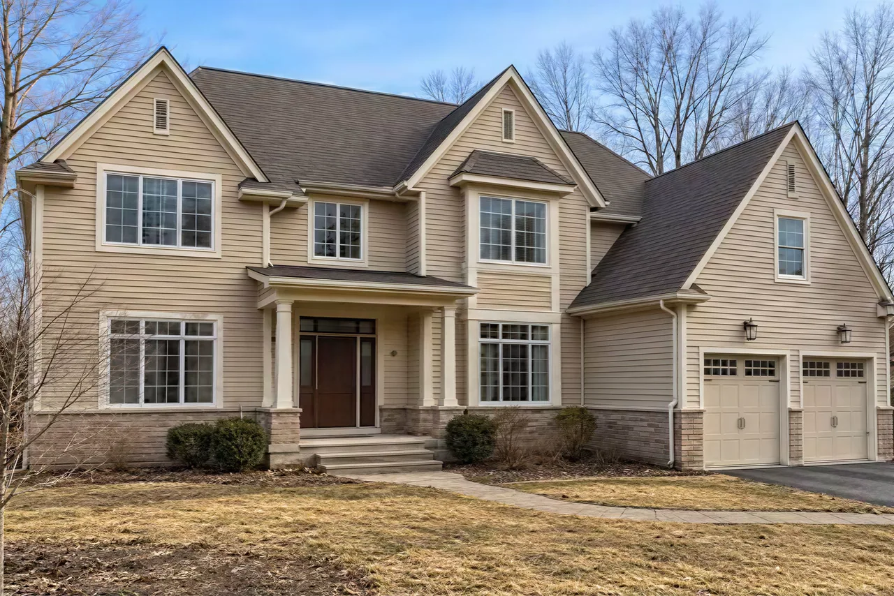 The photo as taken: a tan three-gable two-story house with a dead winter lawn and a few shrubs by the door